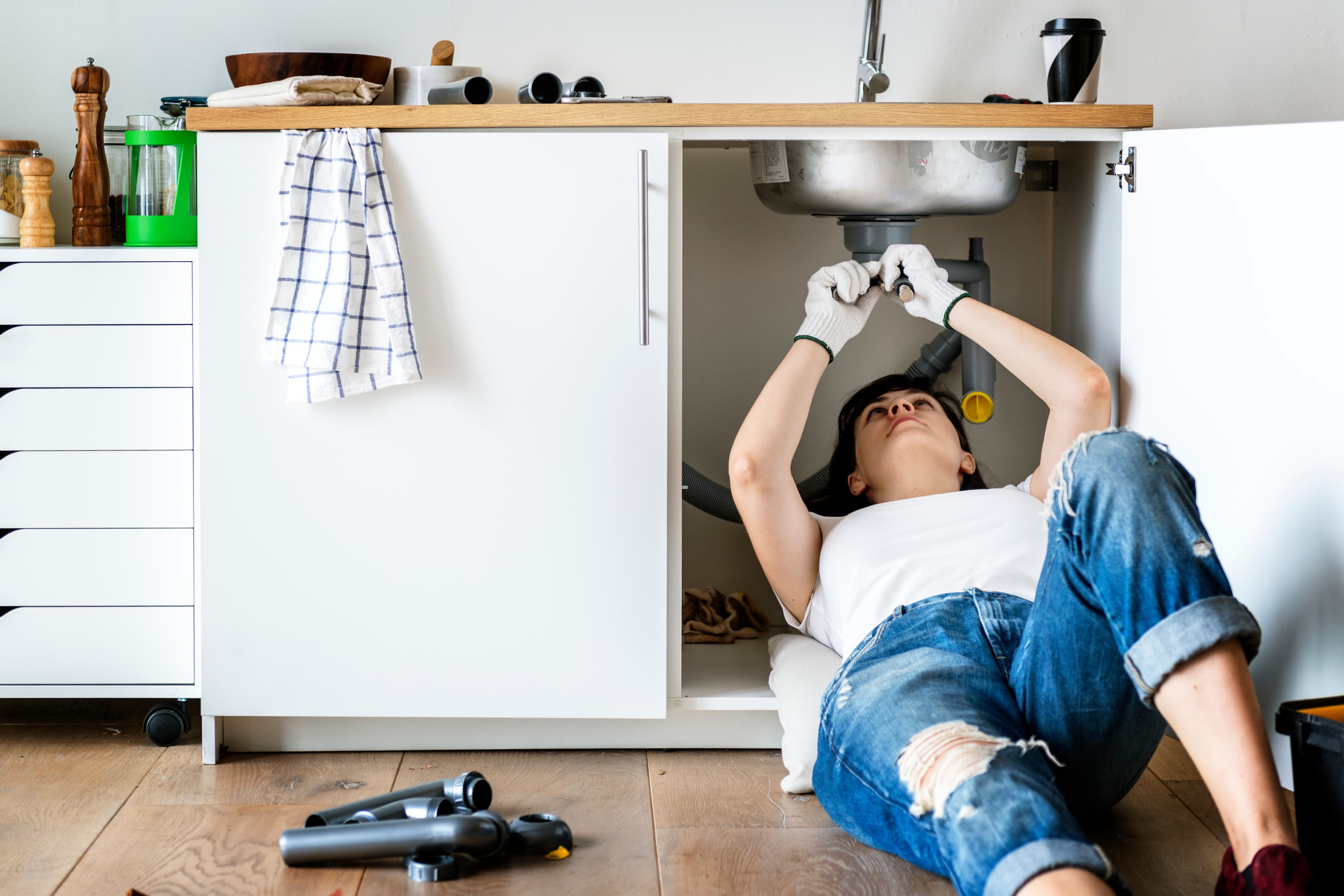 someone using a monkey wrench to tighten a drain pipe underneath a sink.