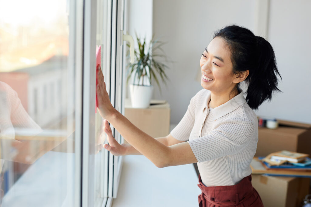Waist up portrait of young woman washing windows while enjoying Spring cleaning in house or apartment, copy space