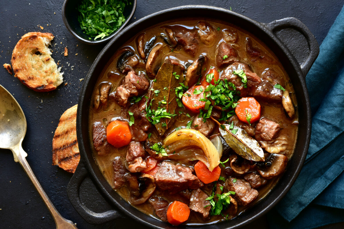 Beef bourguignon - meat stew with vegetables and mushrooms with red wine in a skilet over black slate, stone or concrete background , traditinal dish of french cuisine. Top view with copy space.