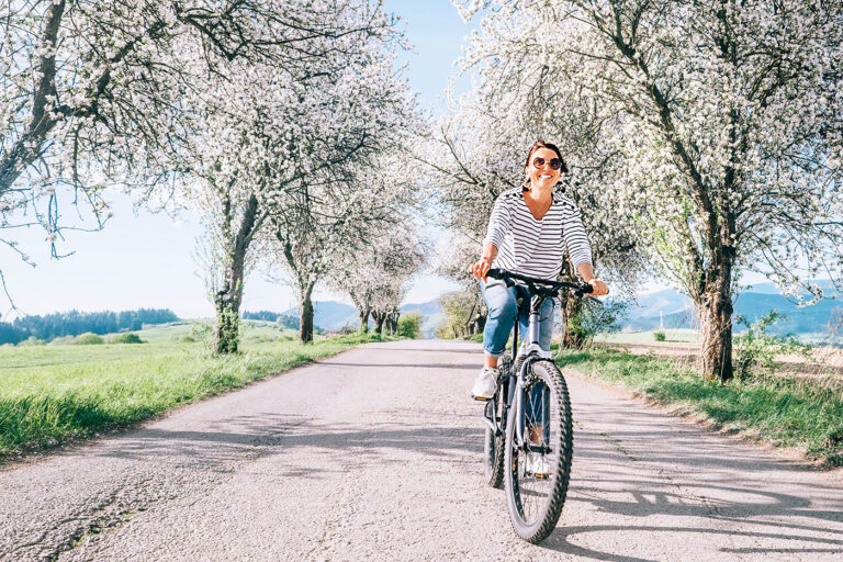 Happy smiling woman rides a bicycle on the country road under bl