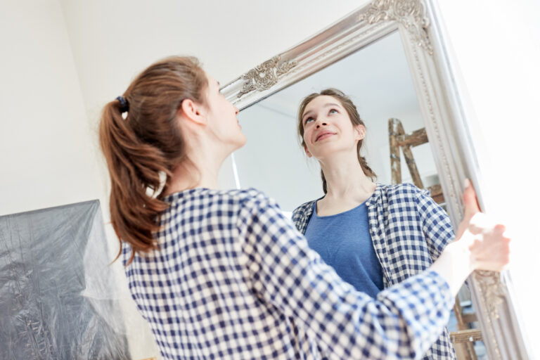 Young woman hanging a mirror in her new home