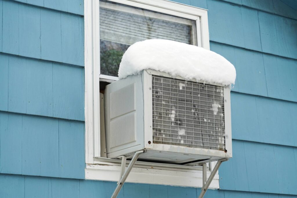 Window air conditioner with snow buildup outside a home during winter weather