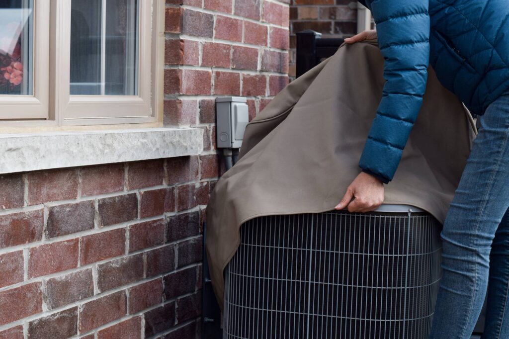 Person placing a protective cover over an outdoor air conditioning unit for winterization”