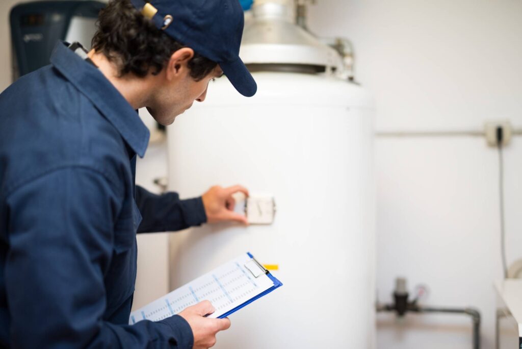 Technician inspecting a home water heater and adjusting the thermostat.