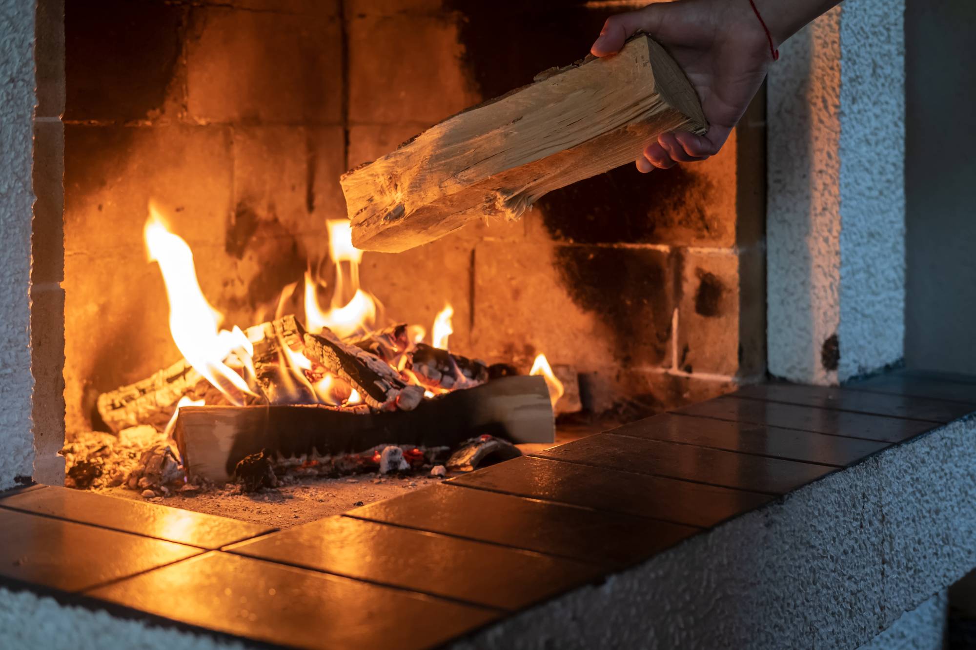 Hand putting a piece of wood into a burning fireplace