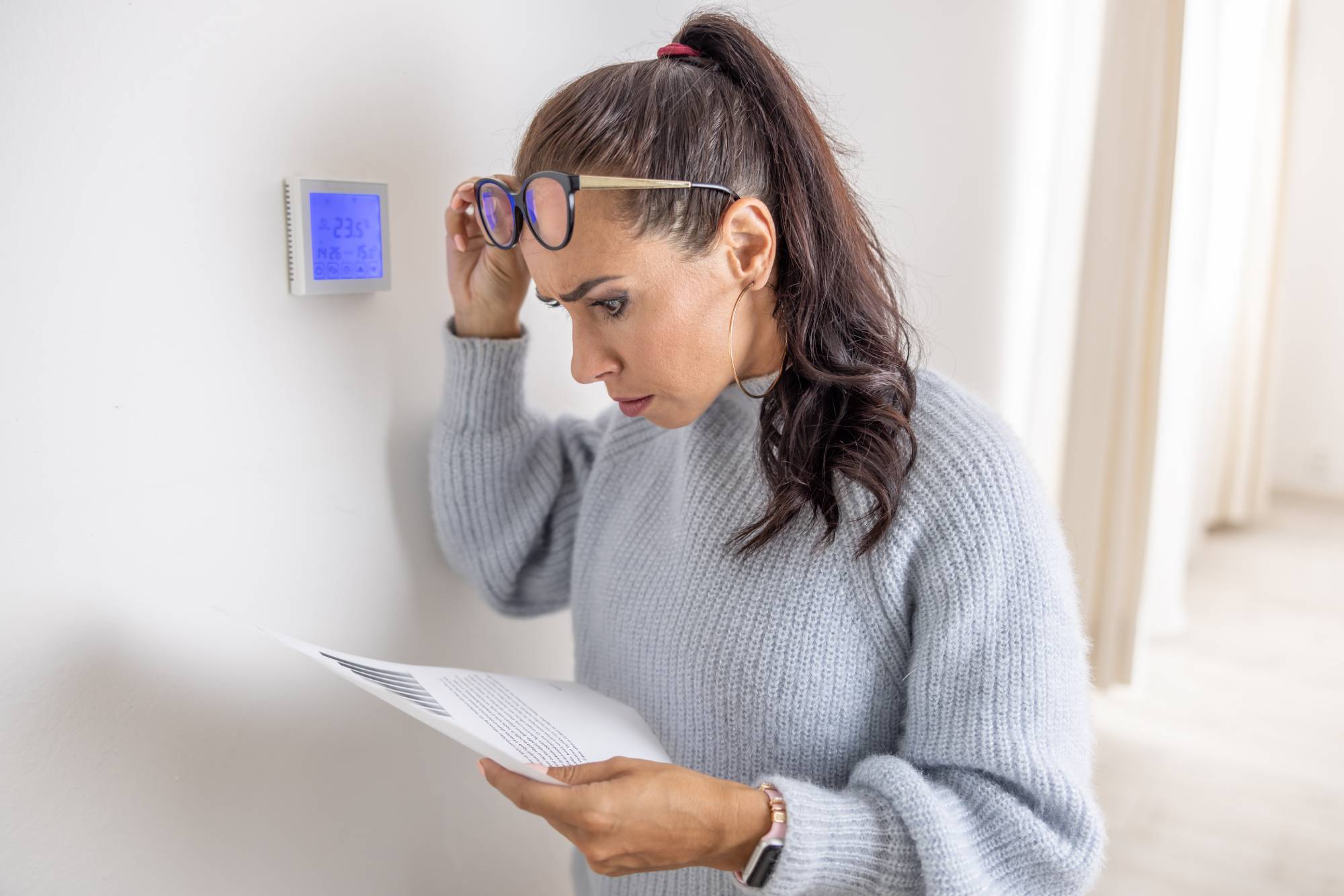Homeowner reviewing heating costs while checking thermostat settings