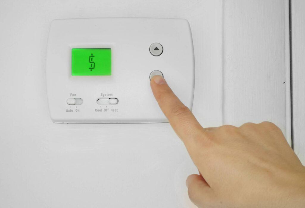 Person lowering a home thermostat to reduce heating costs