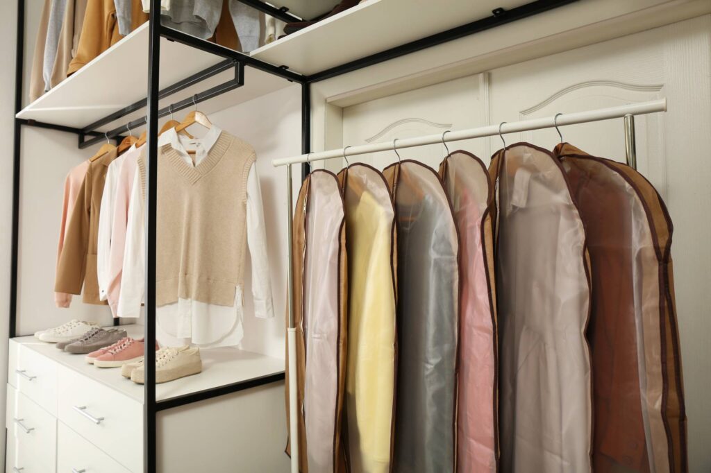 Clothes in garment bags hanging on a clothing hanger in a closet