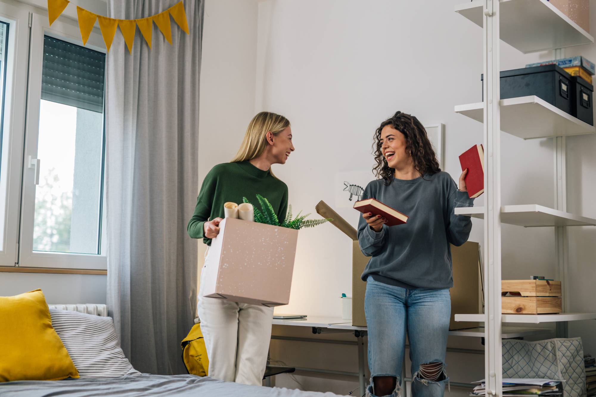 Two college roommates standing in their dorm room unpacking moving boxes