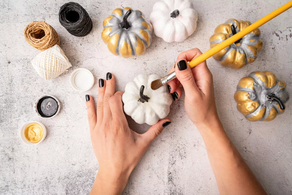 Halloween concept. Halloween DIY craft. Woman hands with a paintbrush coloring pumpkins for a holiday flat lay top view