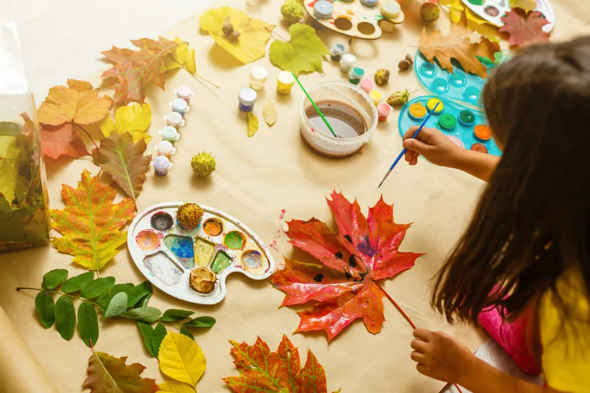 Girl paints leaves. Gouache, brush and various autumn leaves, Children's art project. Colorful Hand-painted on dry autumn leaves